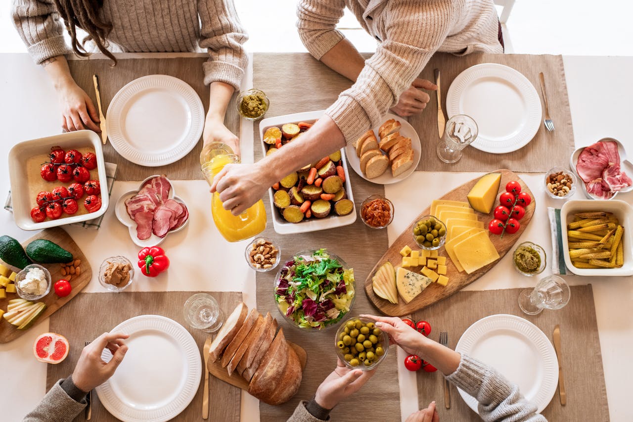 Aerial shot of a diverse brunch spread on a table with multiple hands serving food.