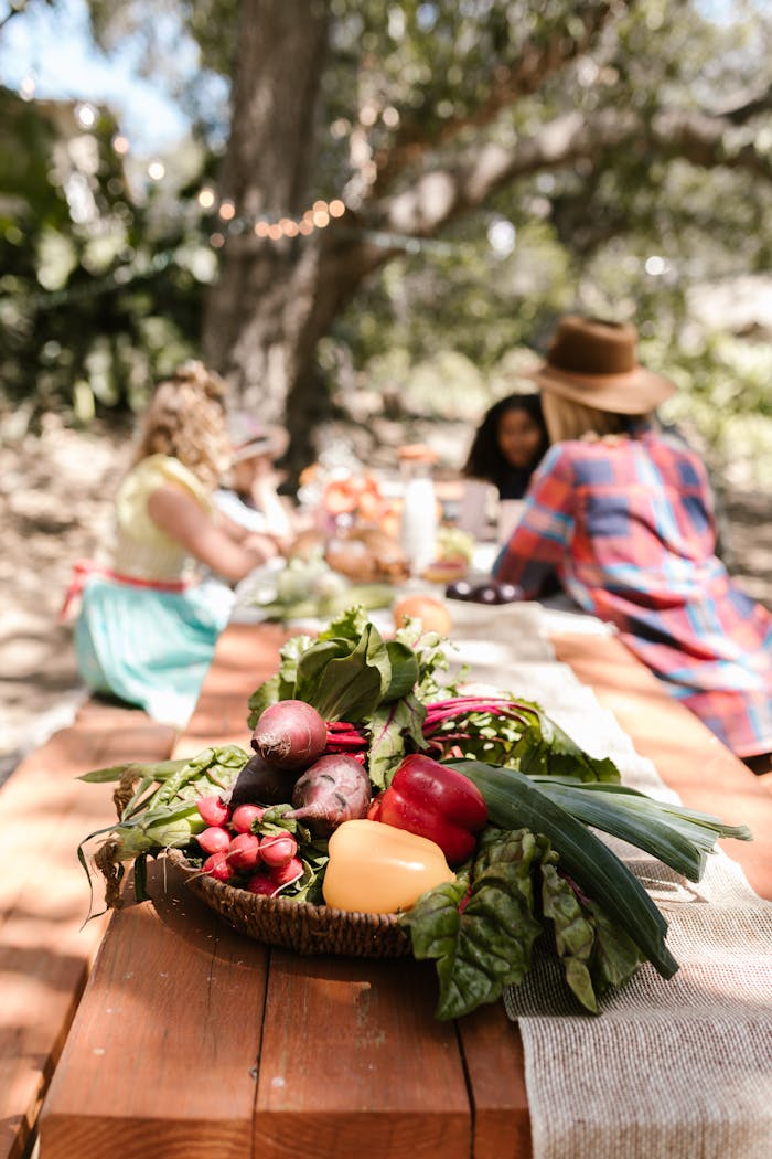 Colorful basket of vegetables on a picnic table with friends outdoors.